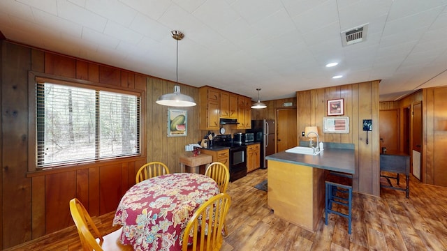kitchen featuring a sink, wooden walls, visible vents, light wood-style flooring, and appliances with stainless steel finishes