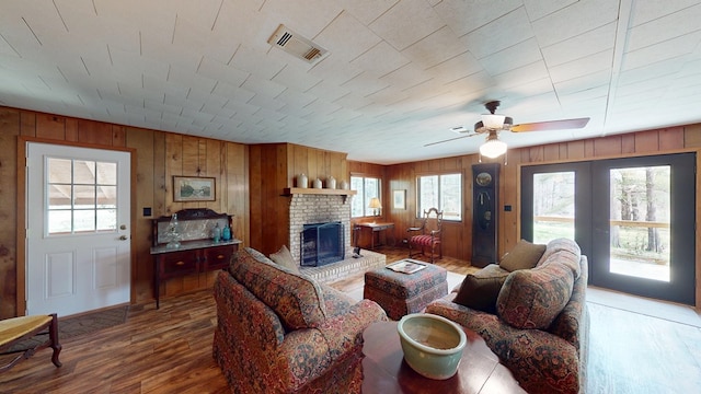 living area featuring wood walls, visible vents, a brick fireplace, wood finished floors, and a ceiling fan