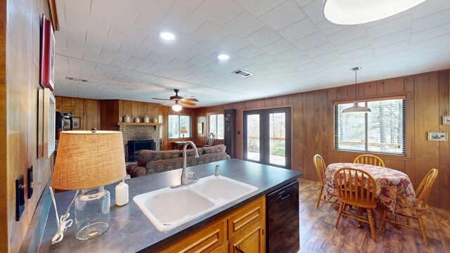 kitchen featuring black dishwasher, a sink, a ceiling fan, brown cabinetry, and wood finished floors