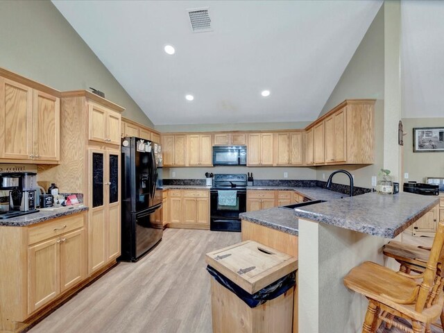 kitchen with visible vents, a breakfast bar, a peninsula, light brown cabinetry, and black appliances