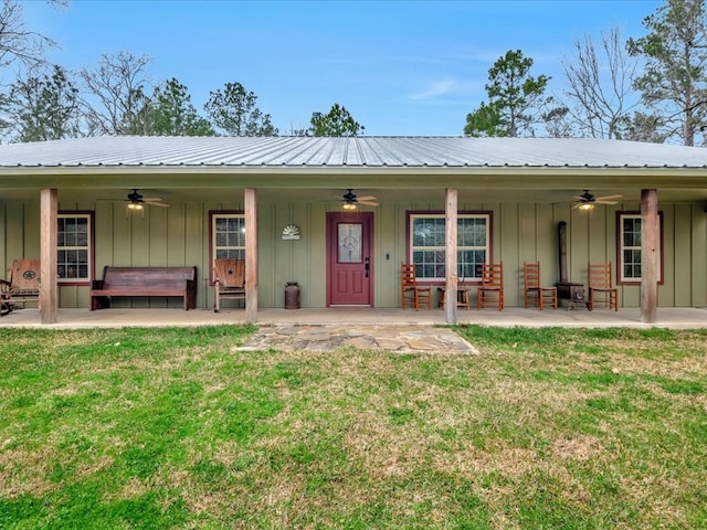 exterior space with board and batten siding, metal roof, a lawn, and a ceiling fan