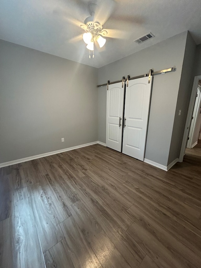 283 Dogwood Rd, Brookeland, TX 75931 - unfurnished bedroom with a barn door, dark wood-style flooring, baseboards, and ceiling fan