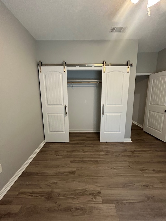 283 Dogwood Rd, Brookeland, TX 75931 - unfurnished bedroom with dark wood-style flooring, baseboards, a closet, and a barn door