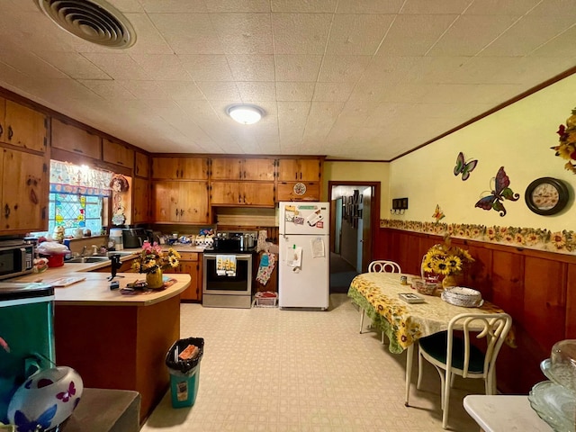 kitchen with appliances with stainless steel finishes, sink, crown molding, and wood walls