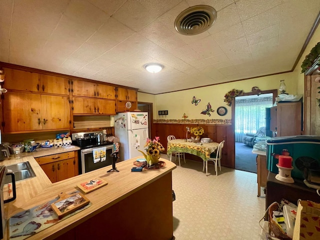 kitchen featuring stainless steel range with electric stovetop, wood walls, sink, white fridge, and kitchen peninsula