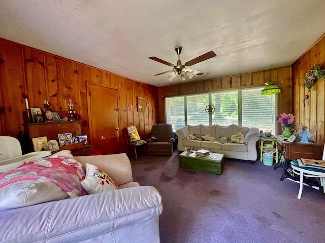 carpeted living room featuring ceiling fan, wood walls, and a textured ceiling