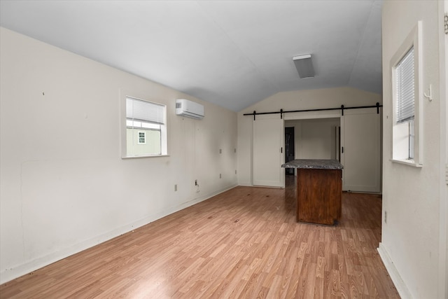 interior space with lofted ceiling, a barn door, a wall unit AC, and light wood-style floors