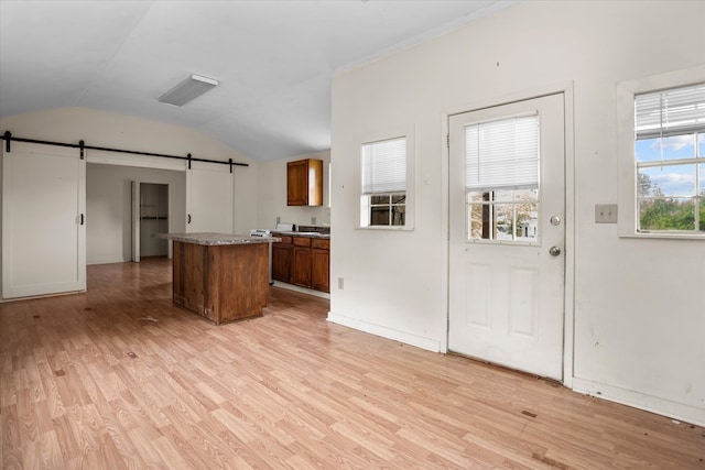 kitchen with a kitchen island, vaulted ceiling, a barn door, and light wood-type flooring