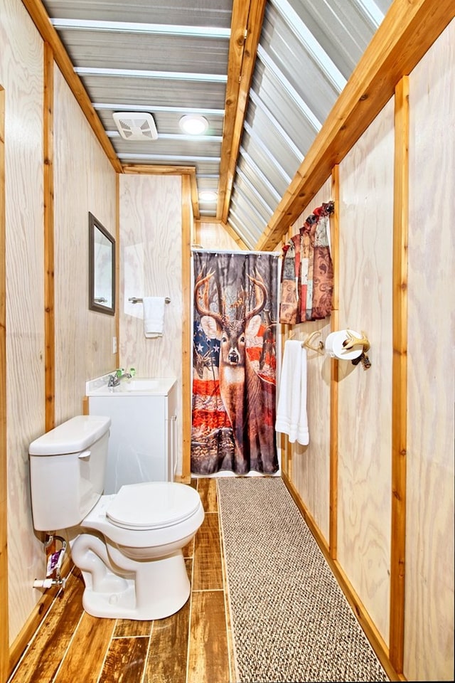 bathroom featuring hardwood / wood-style floors, vaulted ceiling with beams, toilet, and wooden walls