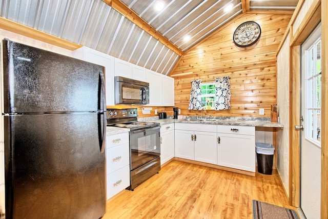 kitchen with white cabinetry, wood walls, vaulted ceiling, black appliances, and light wood-type flooring