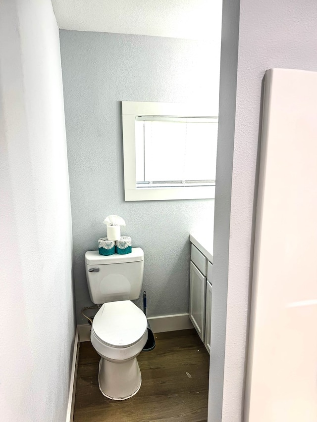 bathroom featuring baseboards, wood finished floors, toilet, vanity, and a textured wall