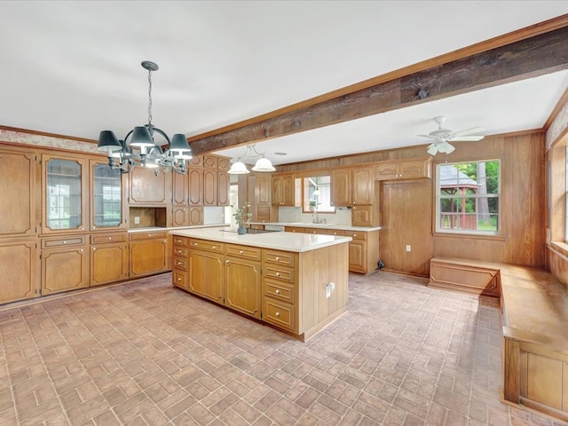 kitchen with beamed ceiling, crown molding, decorative light fixtures, a kitchen island, and ceiling fan with notable chandelier