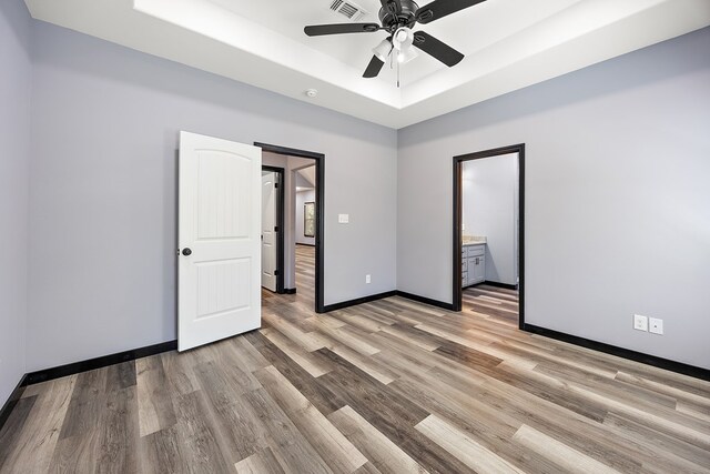 unfurnished bedroom with ceiling fan, light wood-type flooring, connected bathroom, and a tray ceiling