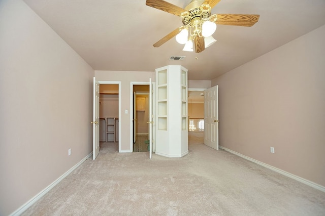 unfurnished bedroom with ceiling fan, light colored carpet, and a walk in closet