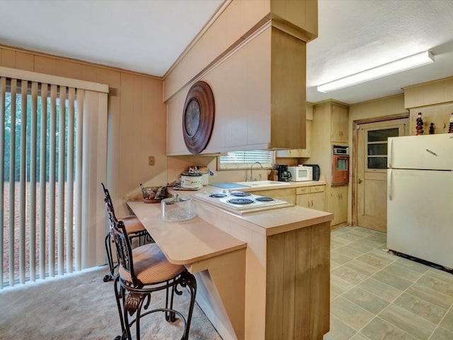 kitchen with kitchen peninsula, a kitchen breakfast bar, light brown cabinetry, white appliances, and sink