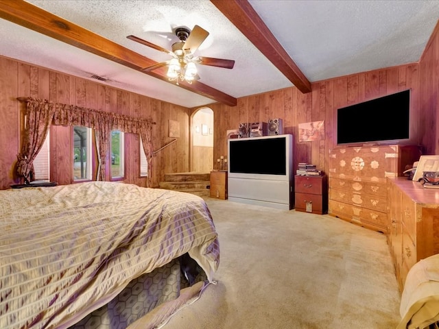 bedroom featuring ceiling fan, wooden walls, beamed ceiling, and light carpet