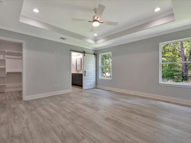 unfurnished bedroom featuring a barn door, a walk in closet, light hardwood / wood-style flooring, and a tray ceiling