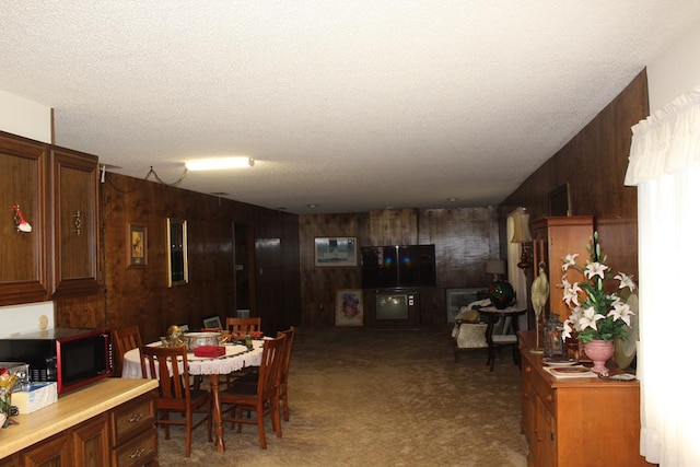 dining room with carpet flooring, a textured ceiling, and wooden walls