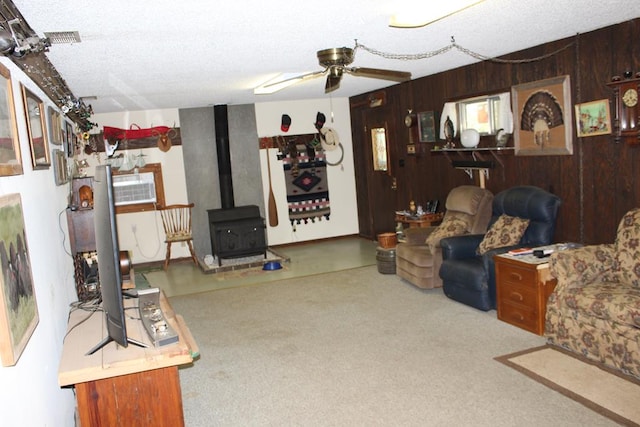 living room with a wood stove, ceiling fan, wood walls, and a textured ceiling