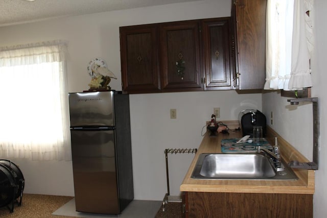 kitchen with stainless steel refrigerator, dark brown cabinetry, and sink