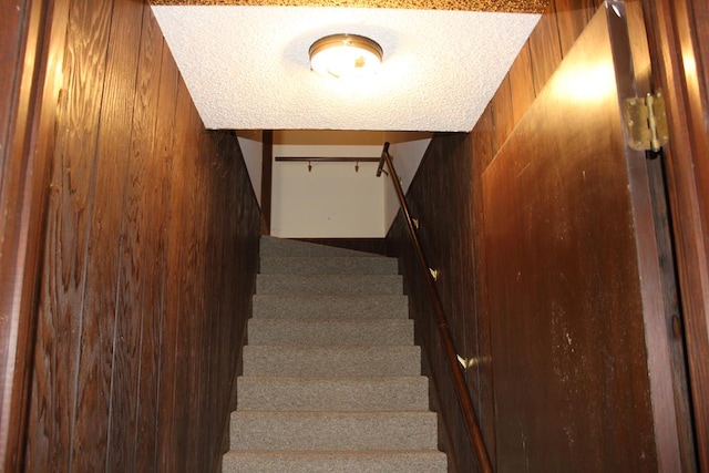 stairs with wooden walls and a textured ceiling