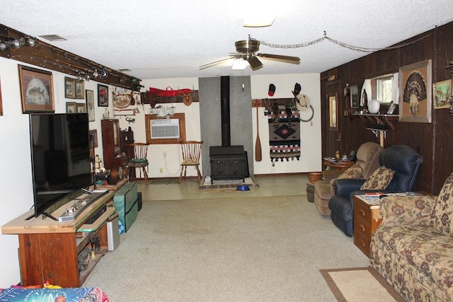 living room featuring a wood stove, wooden walls, ceiling fan, and a textured ceiling