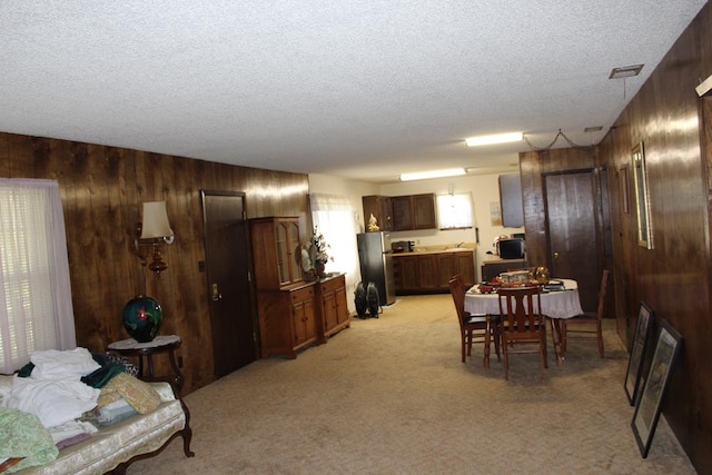 dining space featuring wood walls, light colored carpet, and a textured ceiling