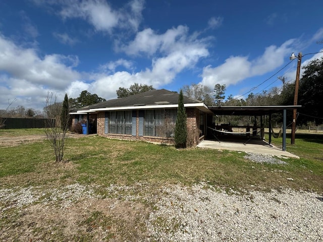 exterior space featuring a carport, a patio area, brick siding, and a lawn