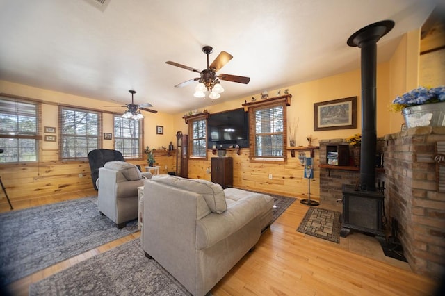 living room with a wood stove, ceiling fan, wood finished floors, and wooden walls