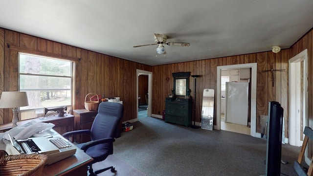 carpeted home office with ceiling fan and wooden walls