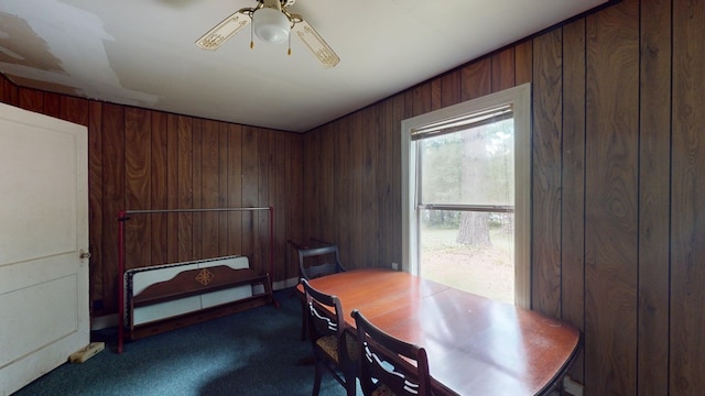 dining space with wooden walls, ceiling fan, and carpet flooring