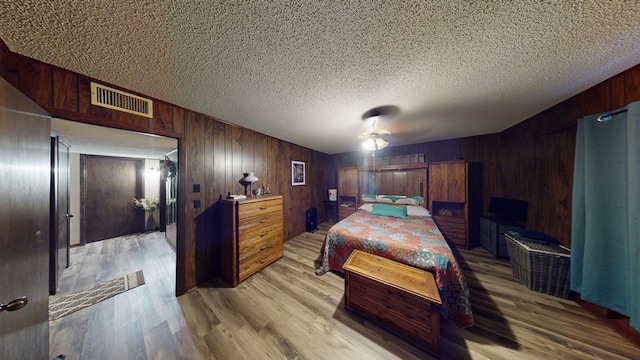 bedroom with ceiling fan, wooden walls, a textured ceiling, and light hardwood / wood-style flooring