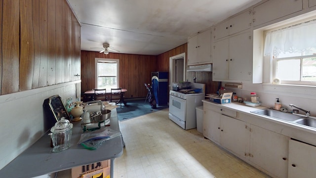 kitchen featuring wood walls, sink, white cabinets, white range with gas stovetop, and ceiling fan