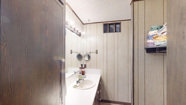 bathroom with ornamental molding, vanity, a textured ceiling, and wood walls