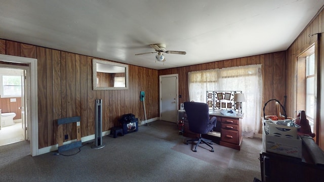 carpeted office space featuring plenty of natural light, ceiling fan, and wood walls