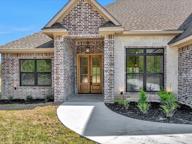 view of exterior entry with french doors, brick siding, and roof with shingles