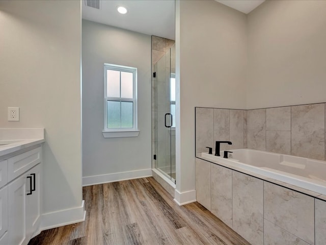 full bathroom with a stall shower, wood finished floors, baseboards, a bath, and vanity