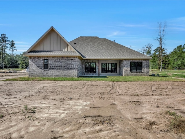 rear view of property with brick siding, board and batten siding, and roof with shingles