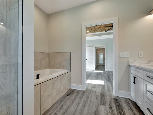 bathroom with tiled tub, hardwood / wood-style floors, and vanity