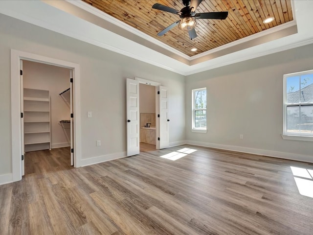 unfurnished bedroom featuring light hardwood / wood-style floors, a walk in closet, multiple windows, and a tray ceiling