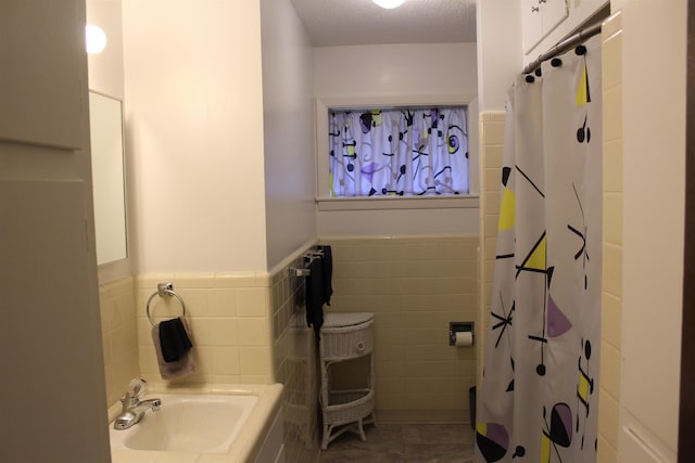 bathroom featuring walk in shower, a textured ceiling, sink, tile walls, and tile patterned flooring