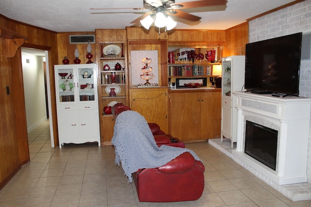 tiled living room with ceiling fan, wood walls, ornamental molding, and a brick fireplace