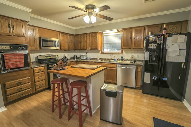 kitchen featuring light wood finished floors, a sink, black appliances, wood counters, and a breakfast bar area