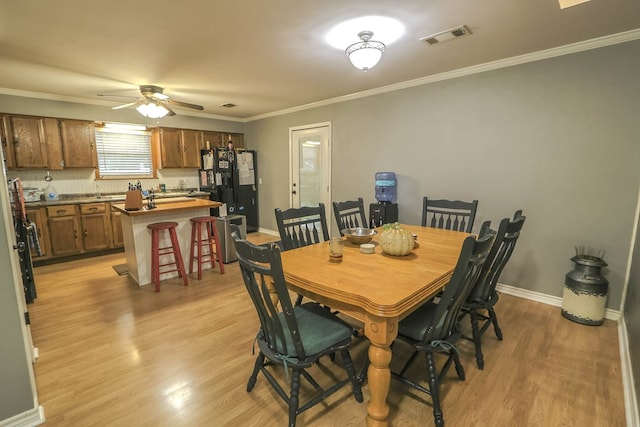 dining space featuring light wood-type flooring, baseboards, visible vents, ceiling fan, and ornamental molding