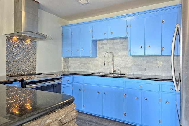 kitchen with wall chimney range hood, sink, dark hardwood / wood-style floors, blue cabinetry, and stainless steel appliances