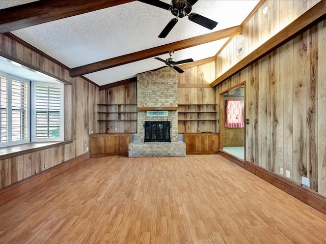 unfurnished living room featuring light wood-type flooring, ceiling fan, wooden walls, lofted ceiling with beams, and a fireplace