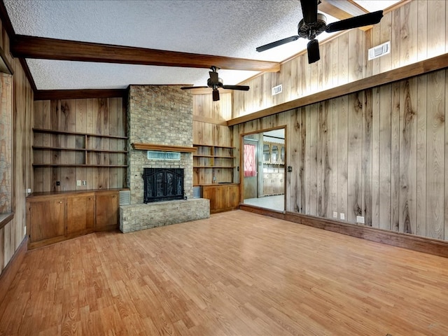 unfurnished living room featuring vaulted ceiling with beams, a textured ceiling, light hardwood / wood-style floors, and wooden walls