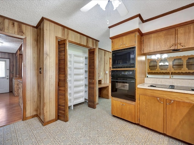 kitchen with ornamental molding, a textured ceiling, wood walls, and black appliances