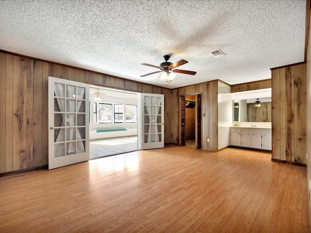 unfurnished living room with light wood-type flooring, wooden walls, and french doors