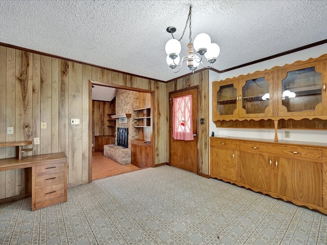 kitchen featuring wood walls, hanging light fixtures, ornamental molding, a textured ceiling, and a notable chandelier